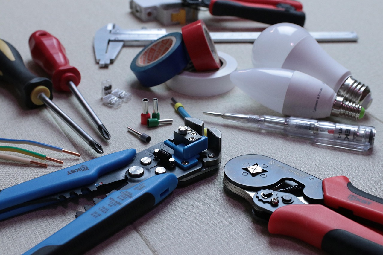 an electrician's screwdrivers, wire strippers, crimpers and tape laid out beside two LED light bulbs